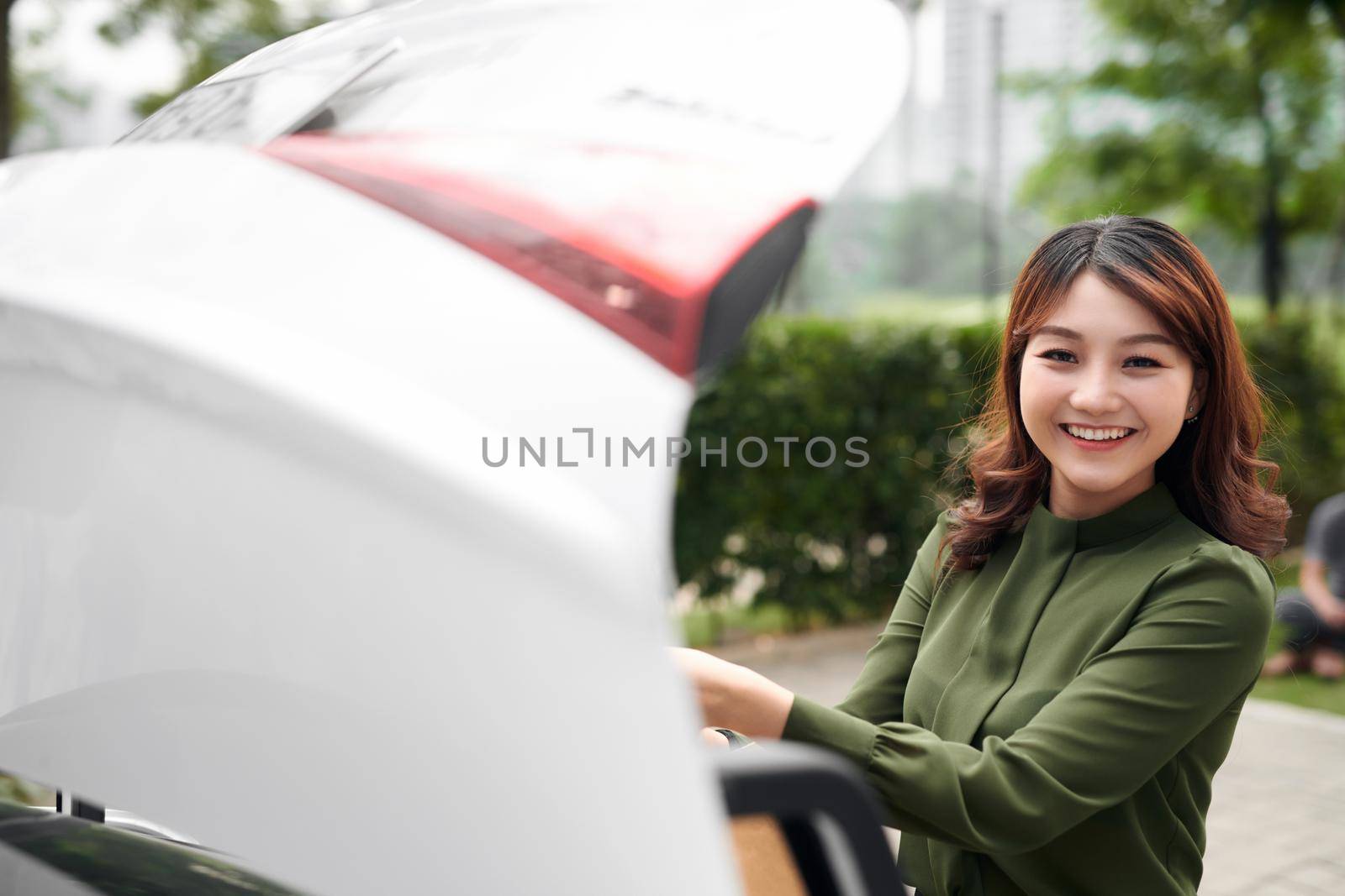 Beautiful girl is putting shopping bags into car trunk and smiling