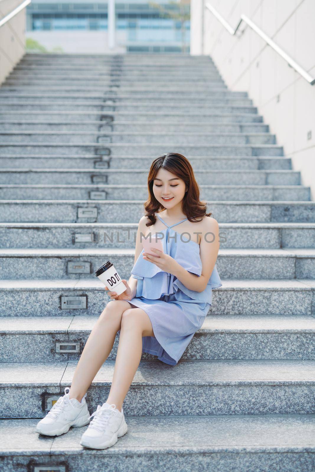 Beautiful young Asian woman sitting at outdoor stair and using smartphone. Lifestyle of modern female.