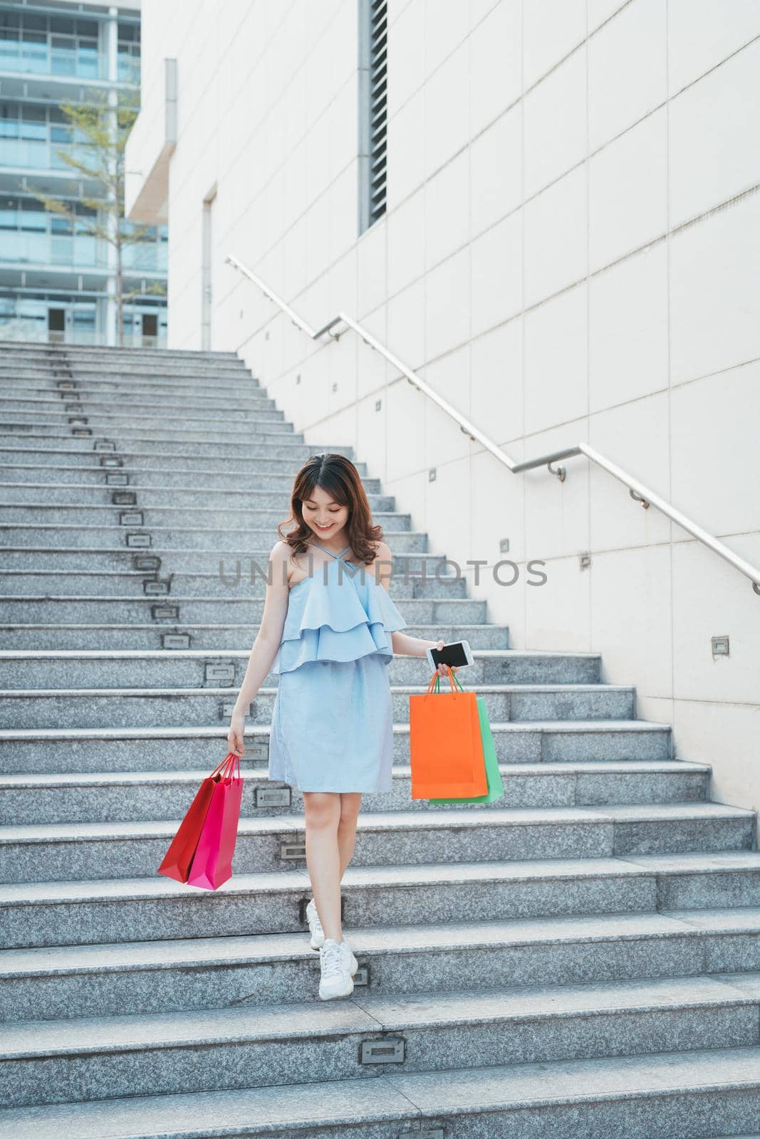 Portrait of young Asian woman going down stairs with color shopping bag. Lifestyle and shopping concept. by makidotvn