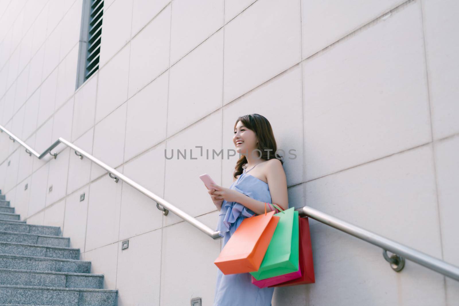 Beautiful young Asian woman with shopping bags outdoors by makidotvn