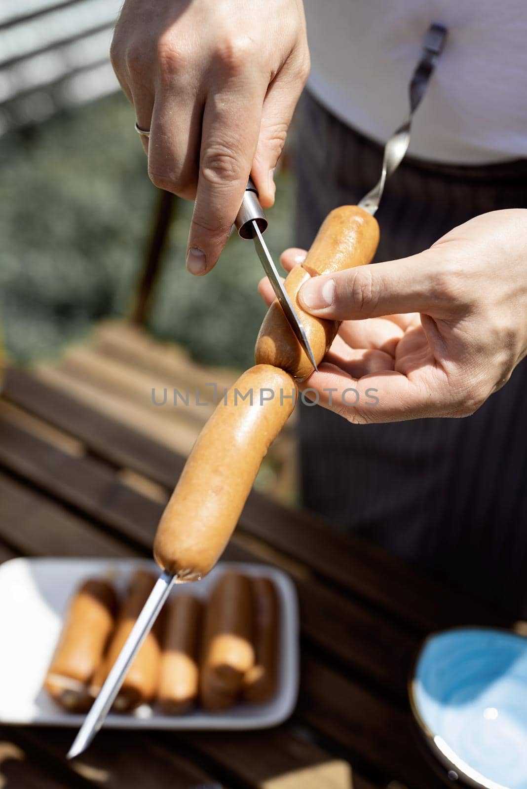 Backyard barbecue. Mans hands grilling sausages and vegetables on metal skewers.