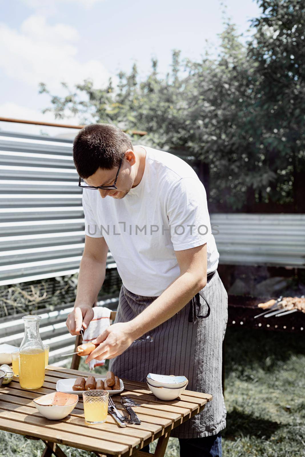 Young man grilling kebabs on skewers, man grilling meat outdoors by Desperada