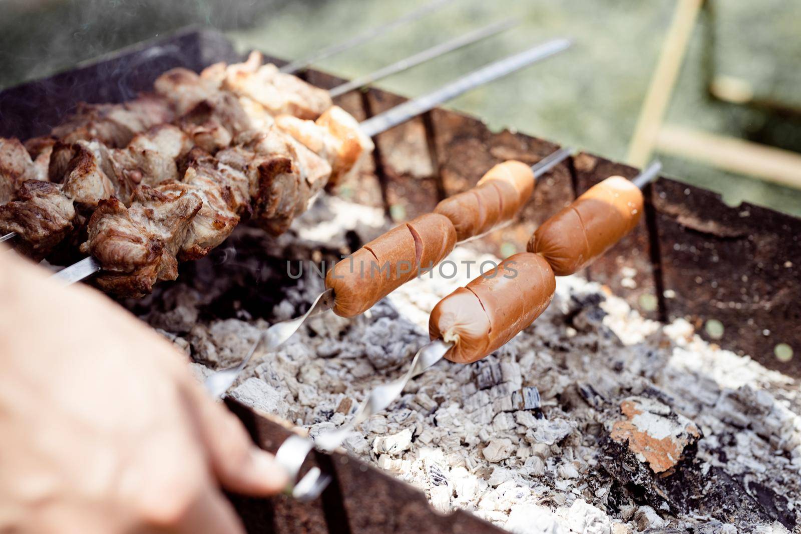 Backyard barbecue. Mans hands grilling kebab and vegetables on metal skewers.