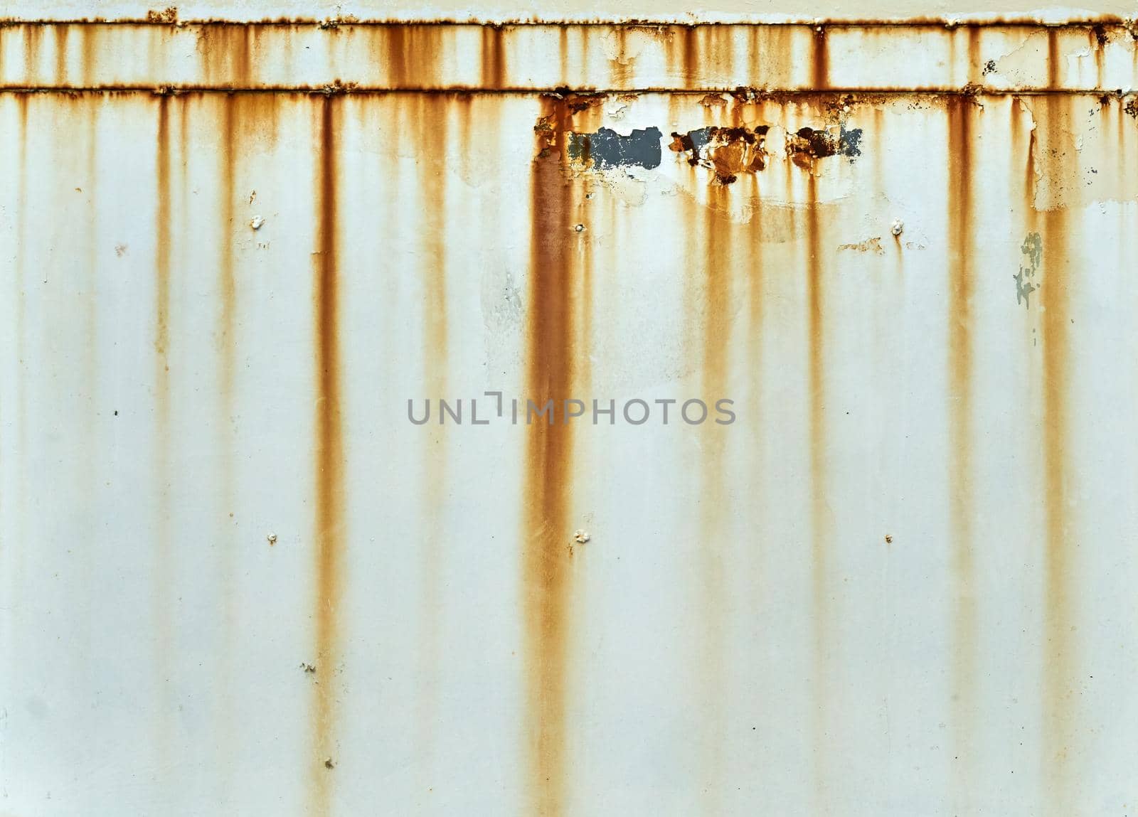 Orange and brown rust stains on a wall of cracked and peeling white paint