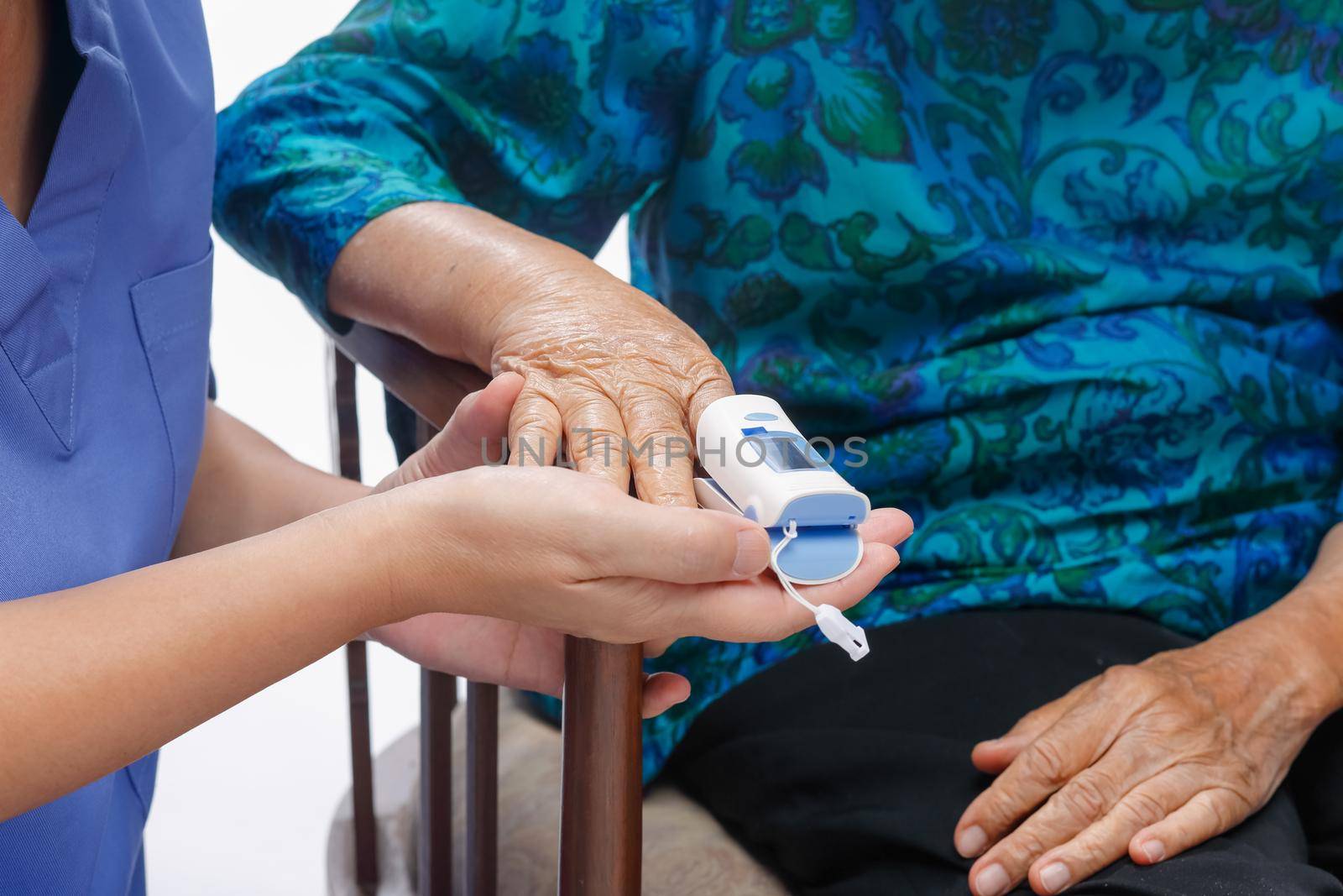 Caregiver monitoring oxygen saturation at fingertip of elderly woman.