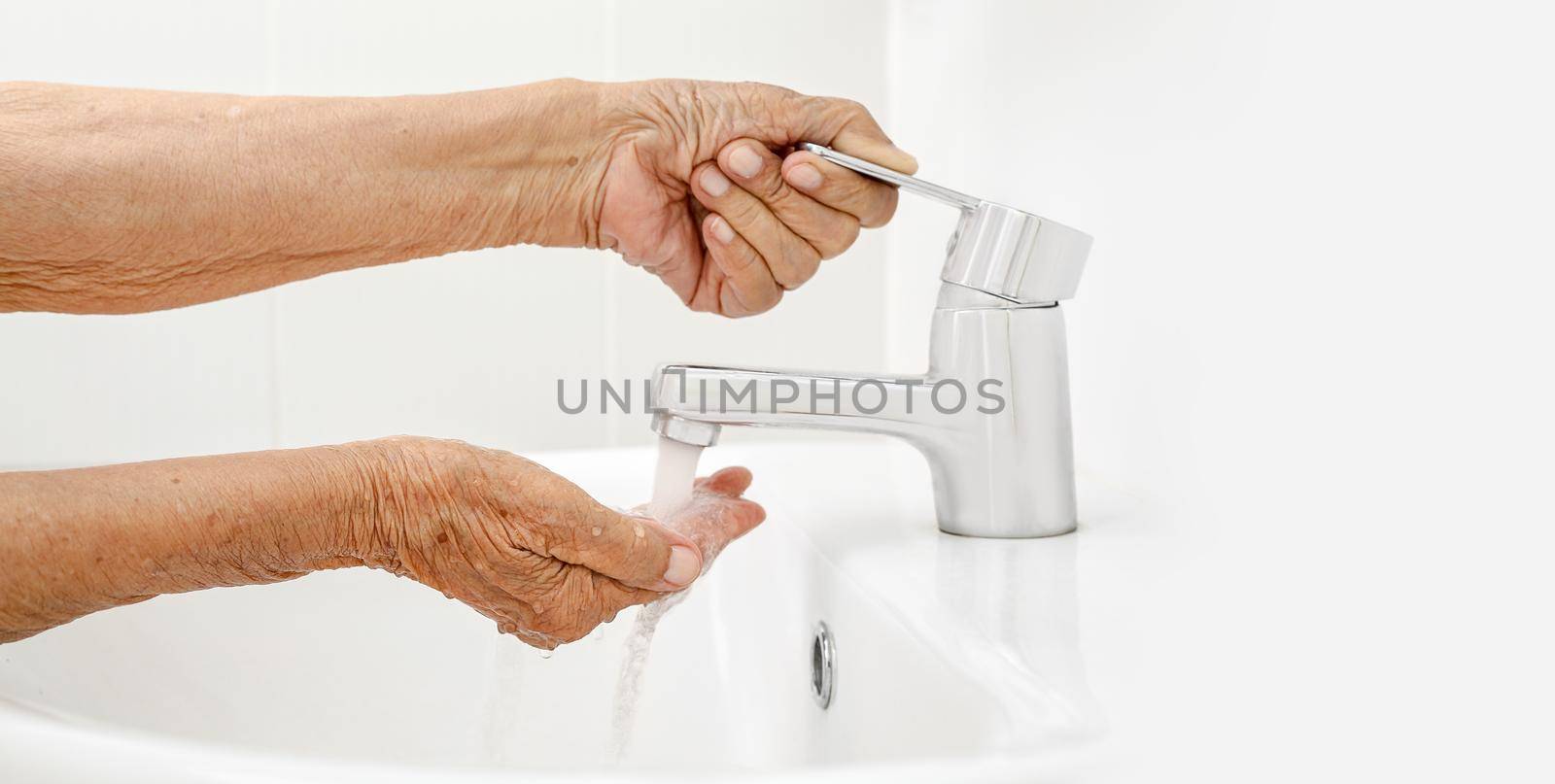 Elderly woman washes hand in bathroom