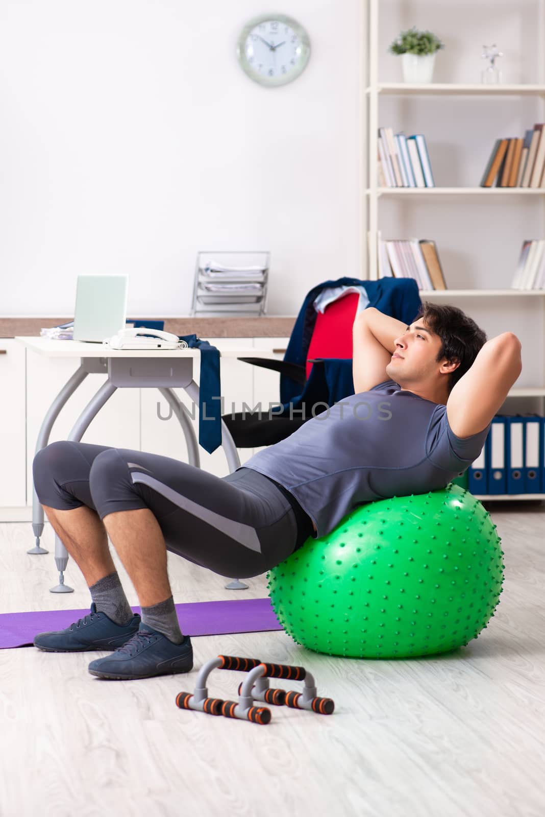 Young male employee exercising in the office by Elnur