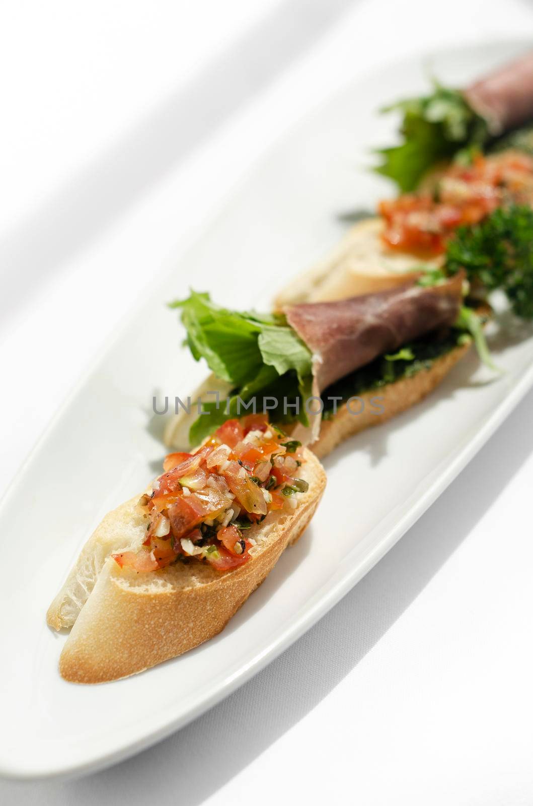 mixed tapas plate with tomato bruschetta and serrano cured ham on white table