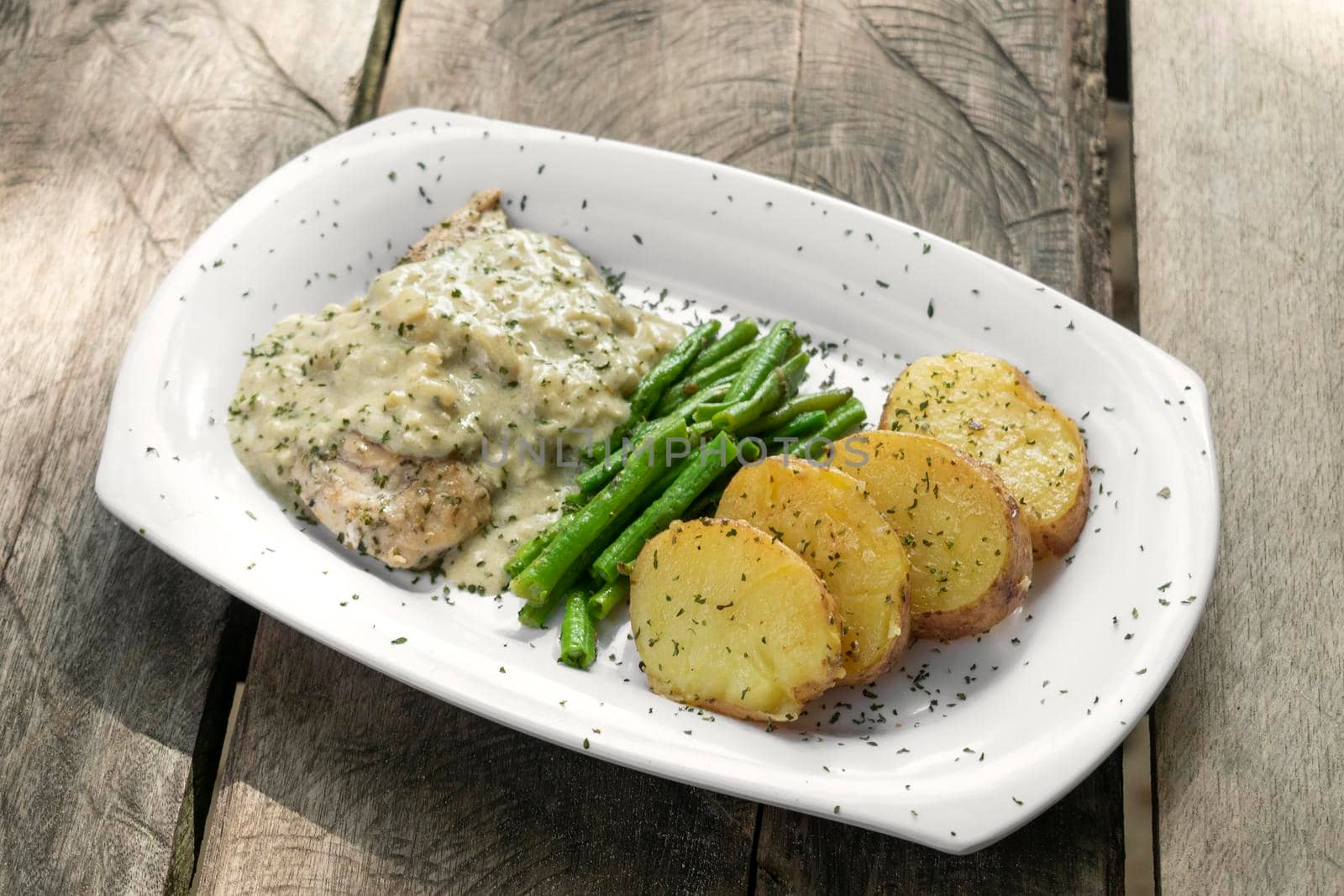 chicken breast with blue cheese sauce and roast potatoes with green beans on rustic old wood background