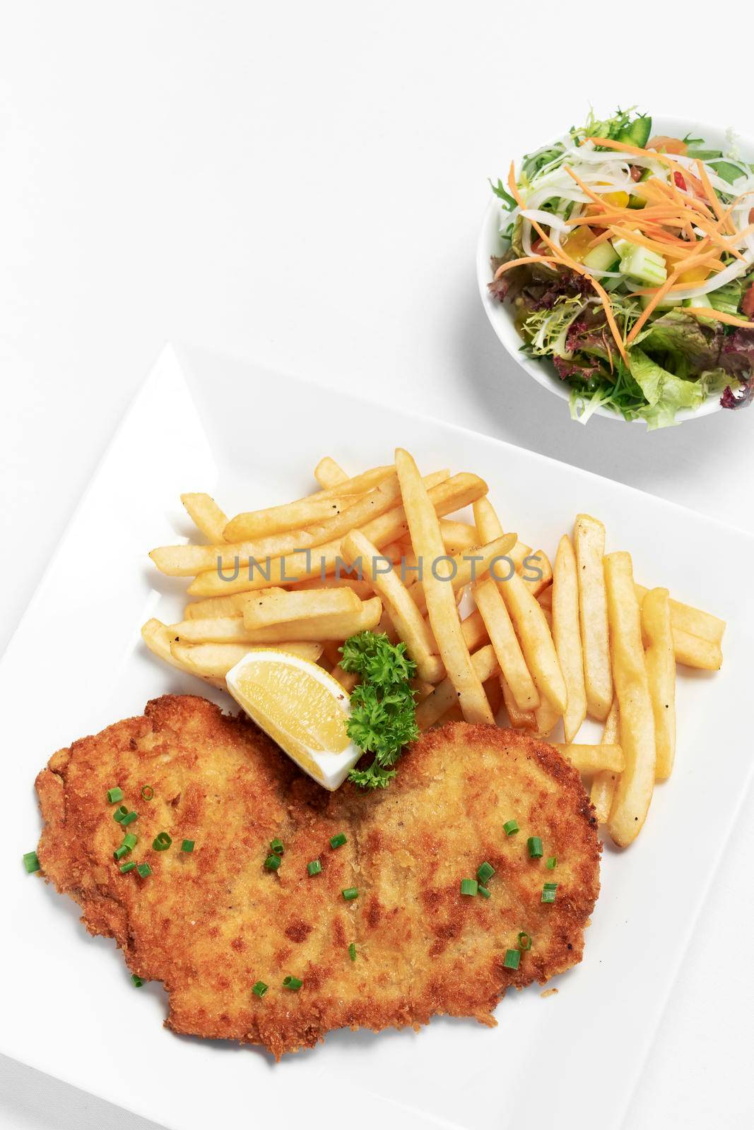 german breaded pork schnitzel with french fries on white studio background