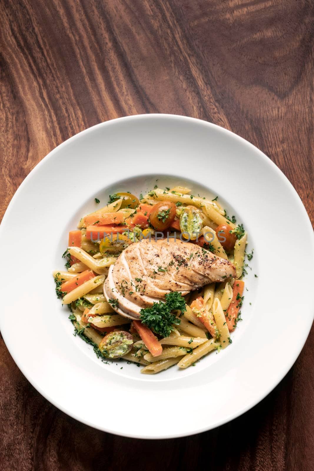 fried chicken breast with penne and saute vegetables pasta dish on wood table background