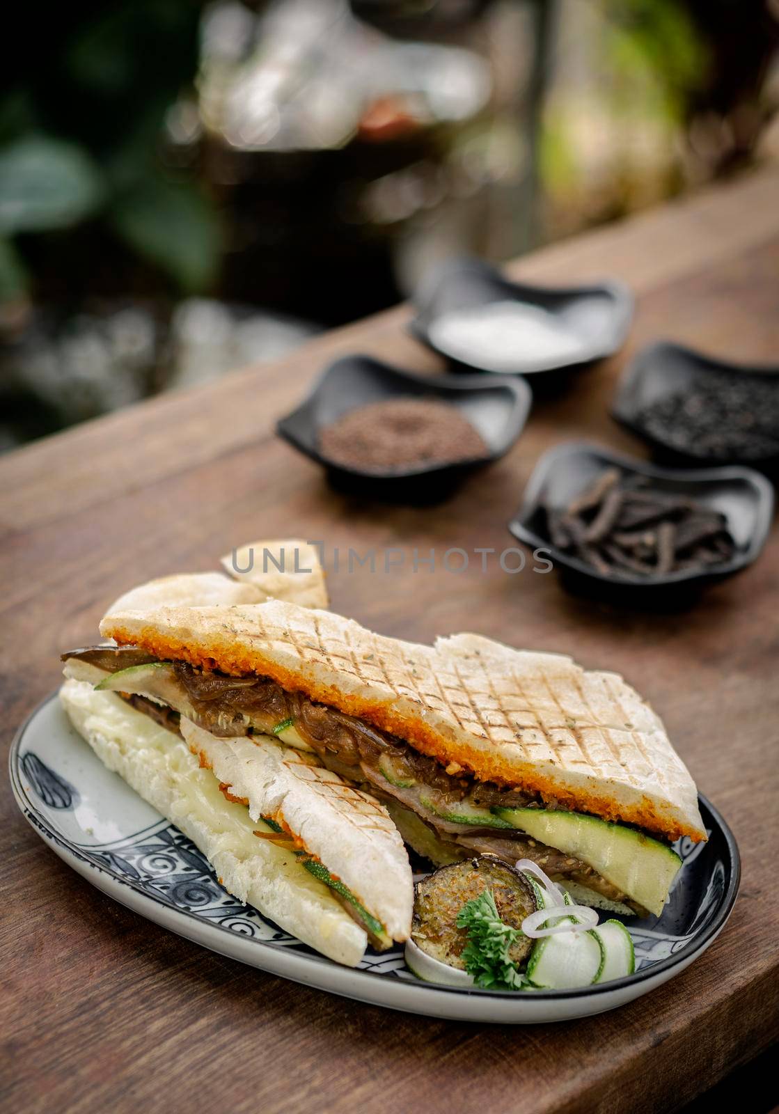 vegan roasted vegetable toasted panini sandwich on wood table outdoors by jackmalipan