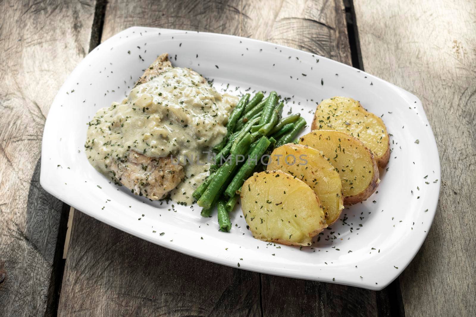 chicken breast with blue cheese sauce and roast potatoes with green beans on rustic old wood background