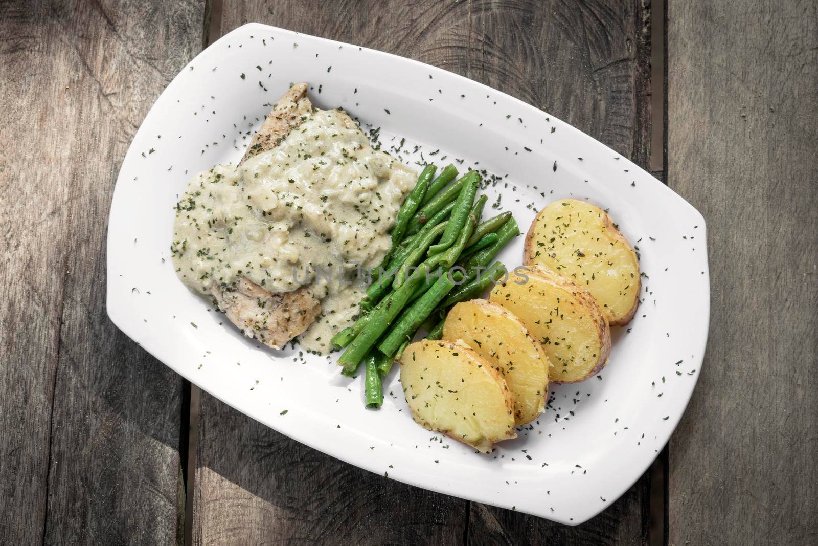 chicken breast with blue cheese sauce and roast potatoes with green beans on rustic old wood background