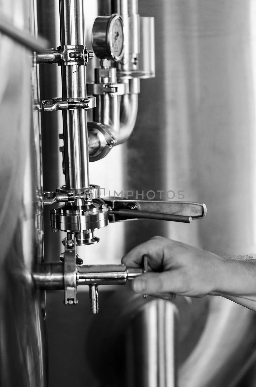 brewer operating industrial beer brewing equipment in brewery interior by jackmalipan