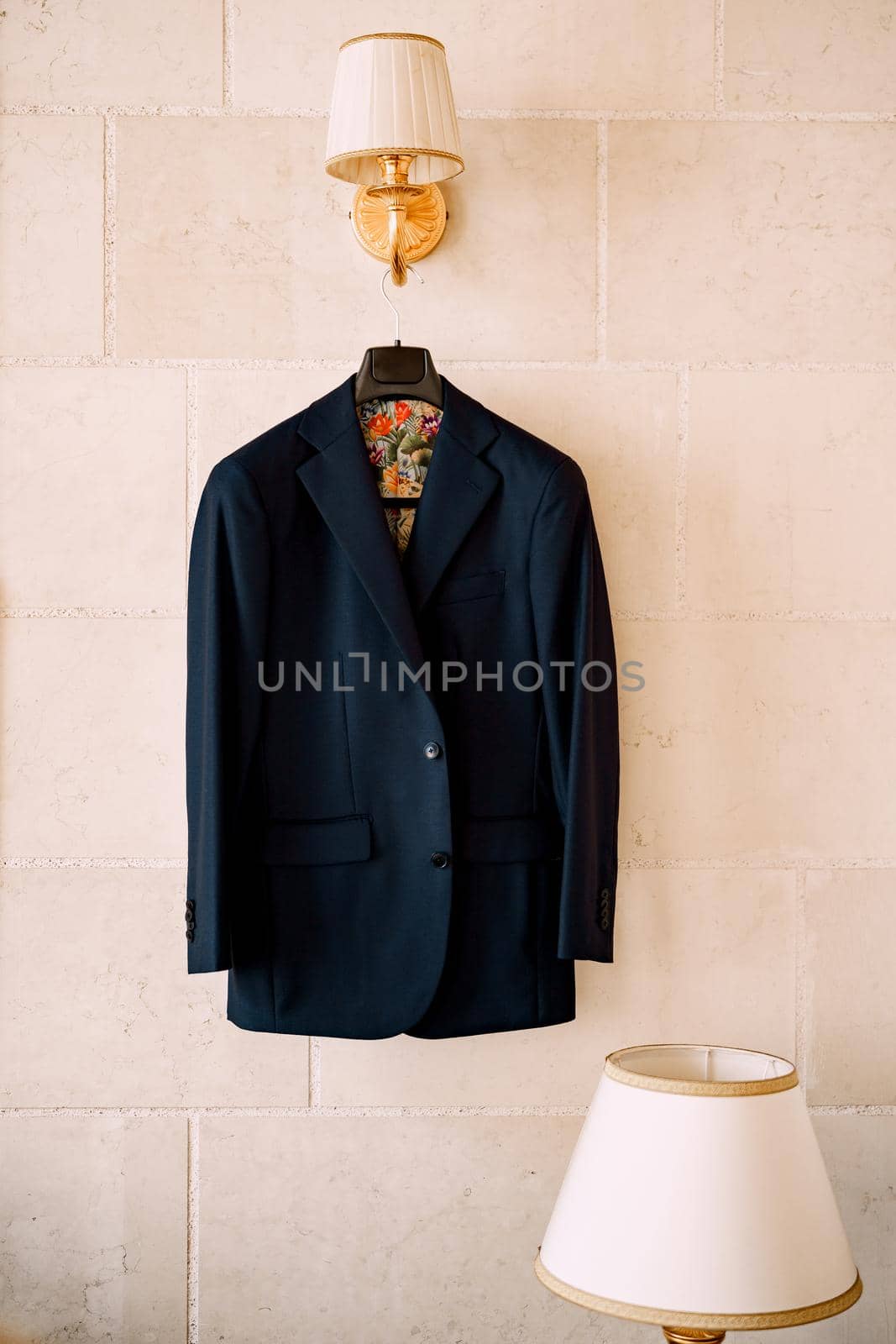 A blue jacket with colorful lining on a black hanger hangs from a wall lamp in a room with a table lamp. High quality photo