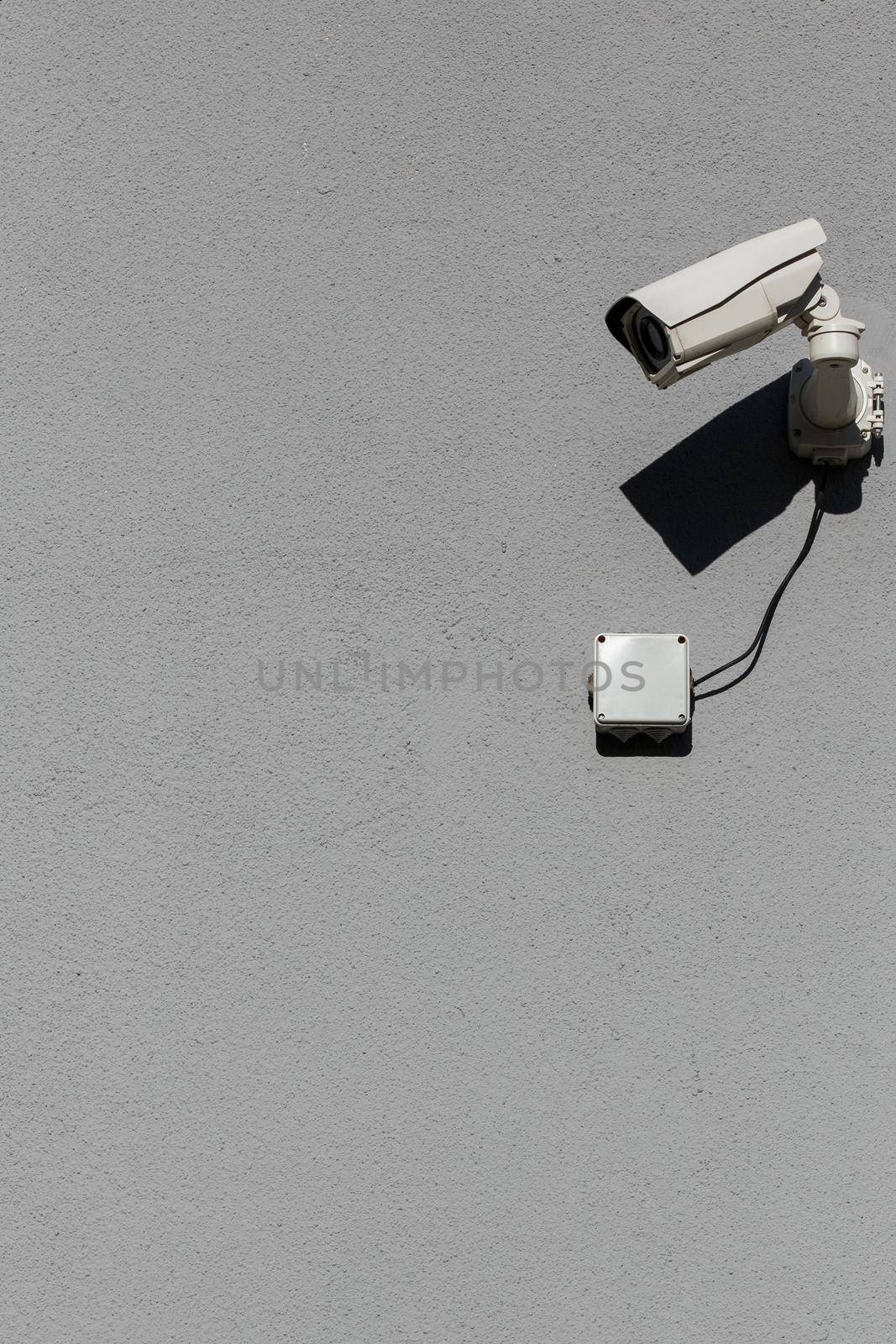 small white surveillance camera on flat gray matte plaster wall pointing sideways