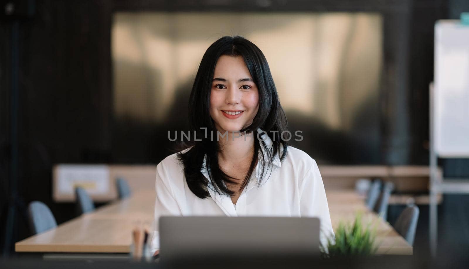 Smiling young asian businesswoman sitting on her workplace in the office. Young woman working at laptop in the office.