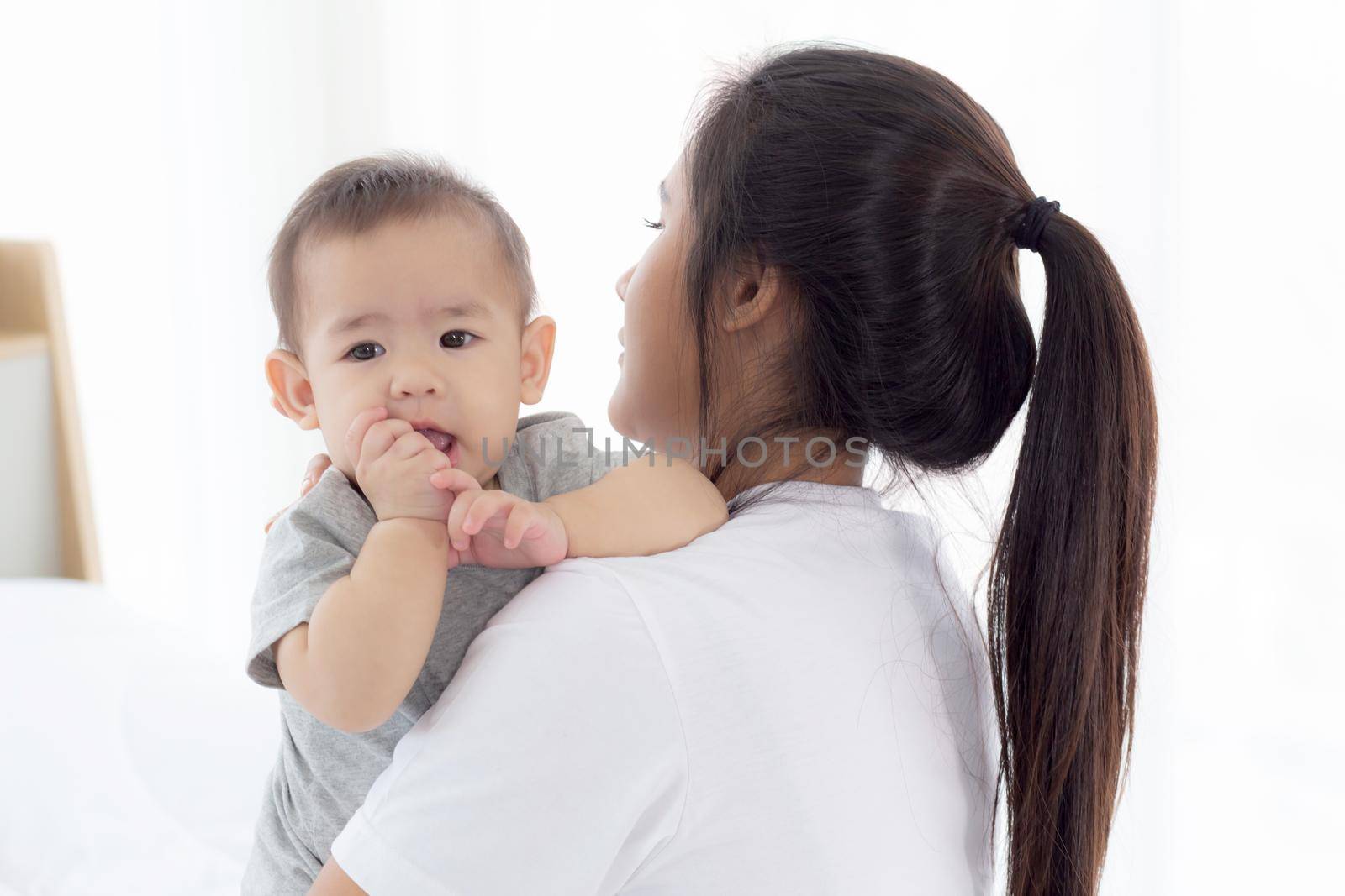 Young asian mother holding little baby girl together in the bedroom at home, mom carry child and care, woman and kid with carefree, toddler and parent, emotion and expression, family concept.