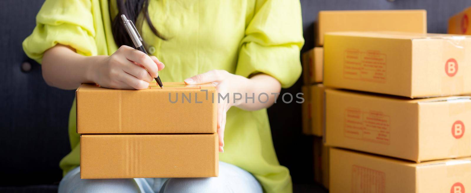 Closeup hand of young asian woman writing address on parcel box at home for delivery order to customer, shipping and logistic, merchant online and seller, business owner or SME, online shopping. by nnudoo