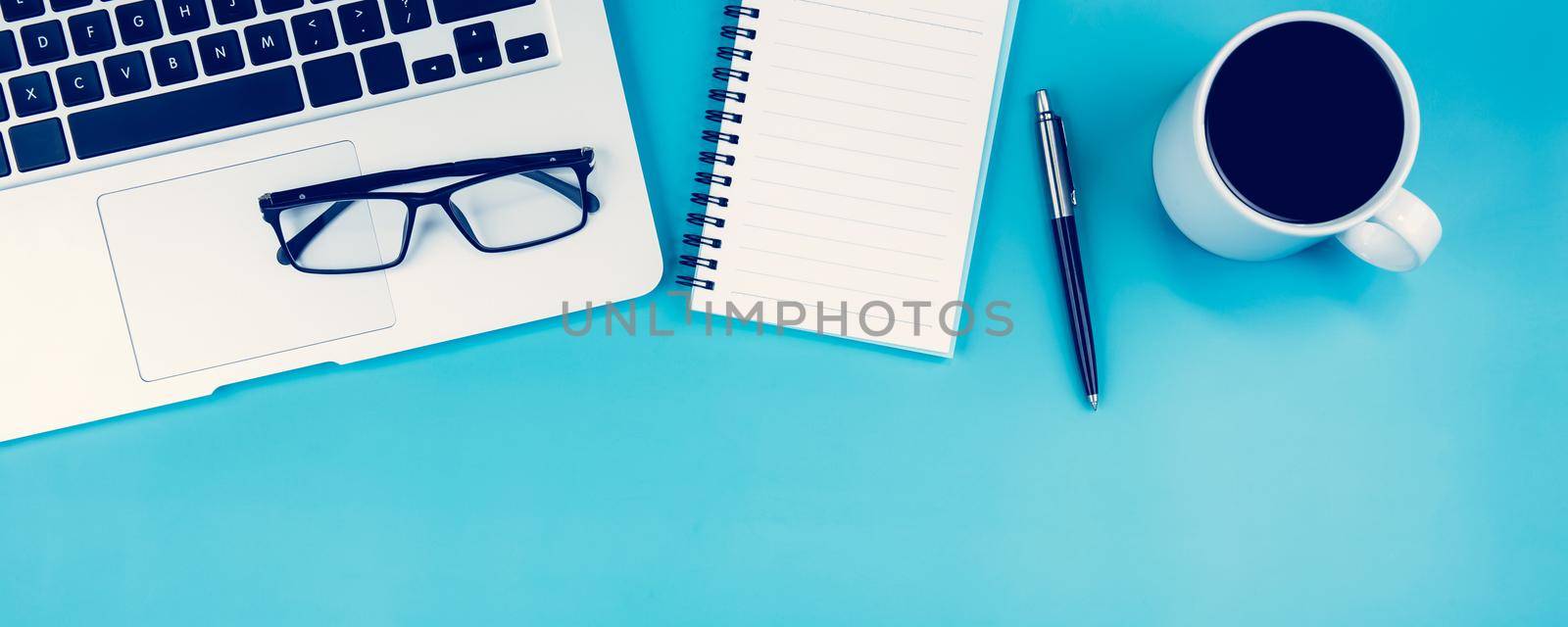 Flat lay of laptop computer and cup of coffee on desk in office, workplace and notebook and glasses and book on blue background, workspace and copy space, top view, business and communication concept.