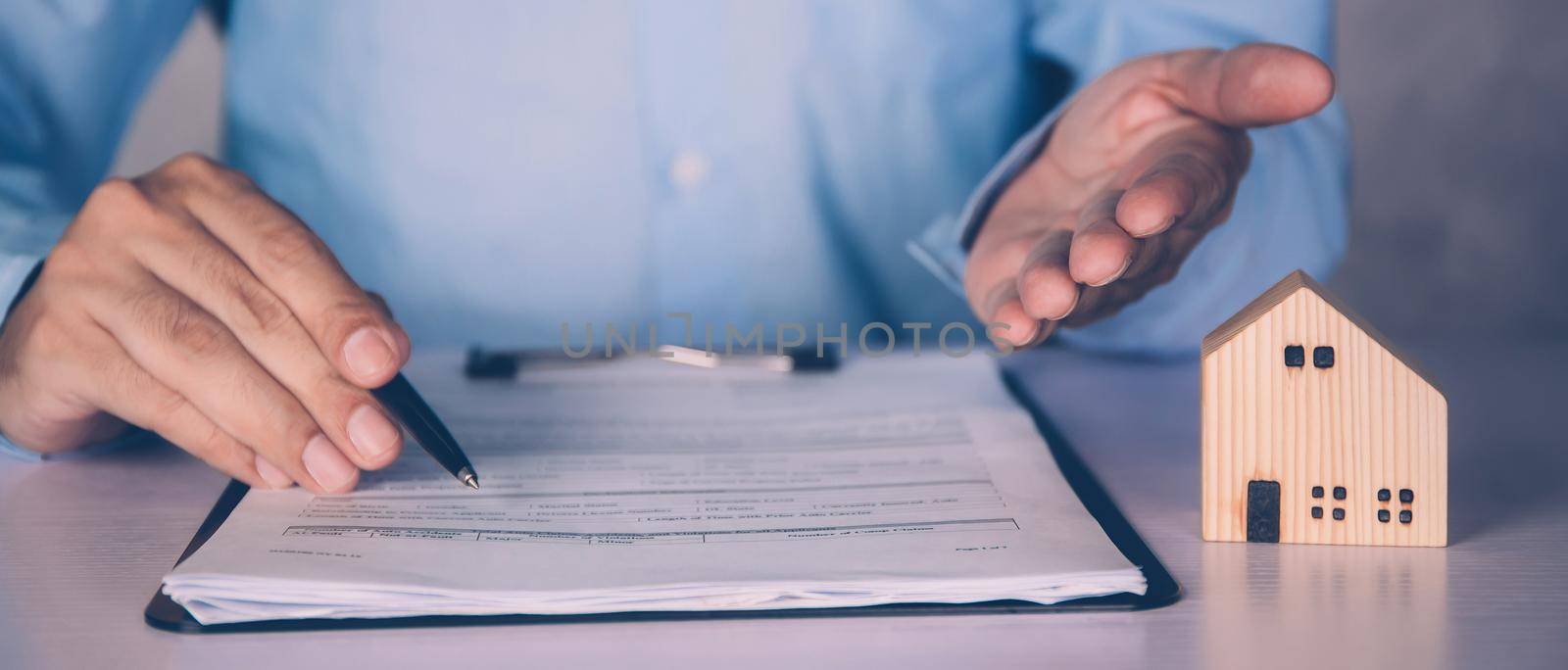 Real estate agent holding home and signing contract about agreement of real property on desk, house broker and planning investment, businessman writing on document form rent house, business concept.