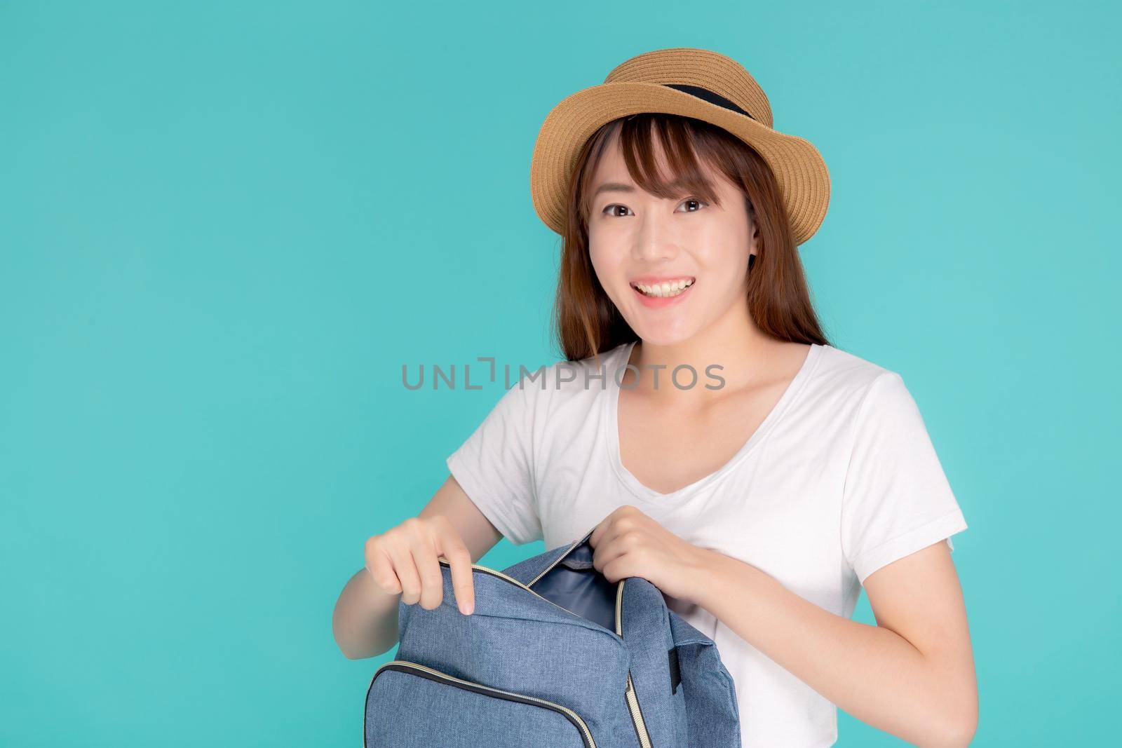Beautiful portrait young asian woman wear hat smiling open backpack travel summer trip holiday in vacation isolated blue background, tourist happy asia girl is cheerful and confident having bag.