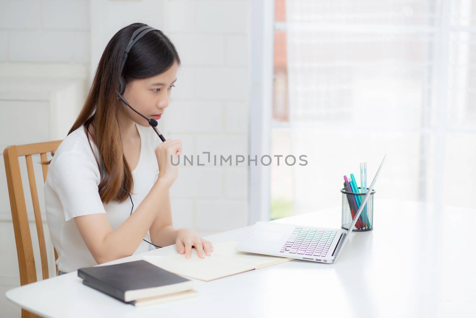 Young asian woman wearing headphone study online with e-learning on desk, girl wearing headset learning to internet with laptop computer at home, new normal, distance education and training.