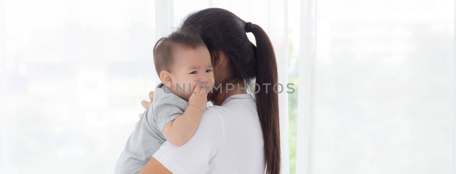 Young asian mother holding little baby girl and walking together in the bedroom at home, mom carry daughter and care, relationship of parent and child, toddler and parent, indoor, family concept.