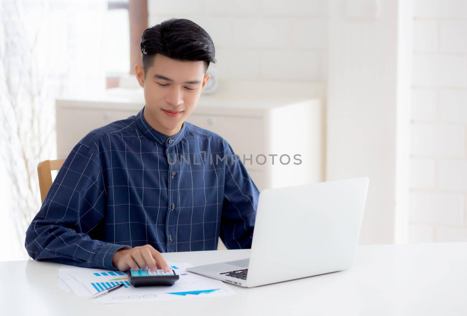 Young asian business man working using calculator for planning accountant, graph for finance and report statistics, investment and profit of income, businessman analyzing expenses with chart.