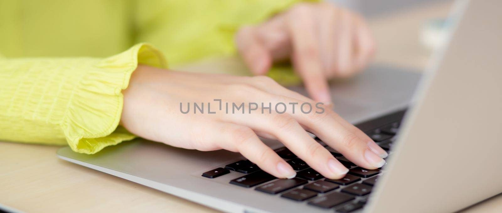 Closeup of hand young asian businesswoman working on laptop computer on desk at home office, freelance looking and typing on notebook on table, woman studying online, business and education concept. by nnudoo