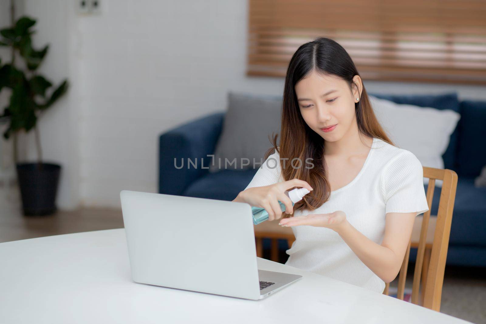 Young asian woman work from home with alcohol gel or sanitizer for cleaning hand and protect coronavirus or covid-19, new normal, quarantine and social distancing, businesswoman using laptop computer.