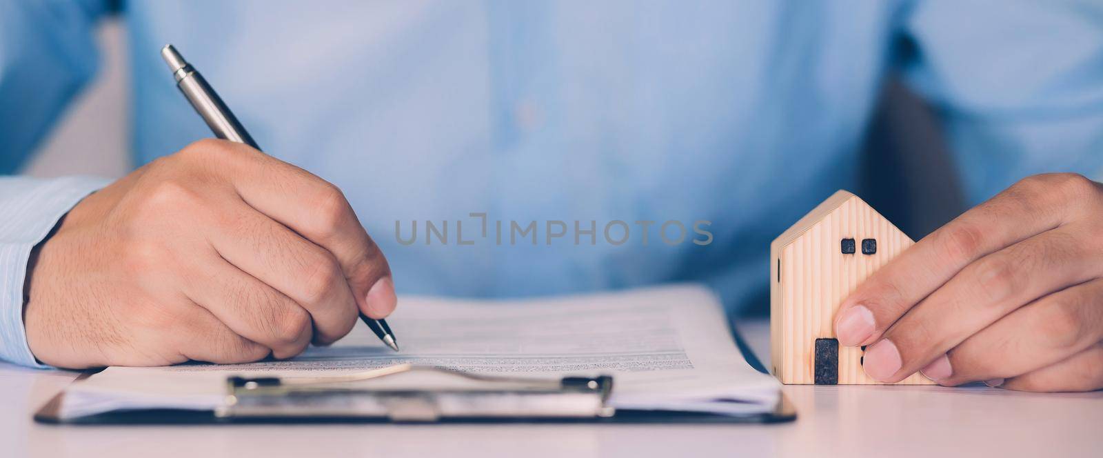 Real estate agent holding home and signing contract about agreement of real property on desk, house broker and planning investment, businessman writing on document form rent house, business concept.