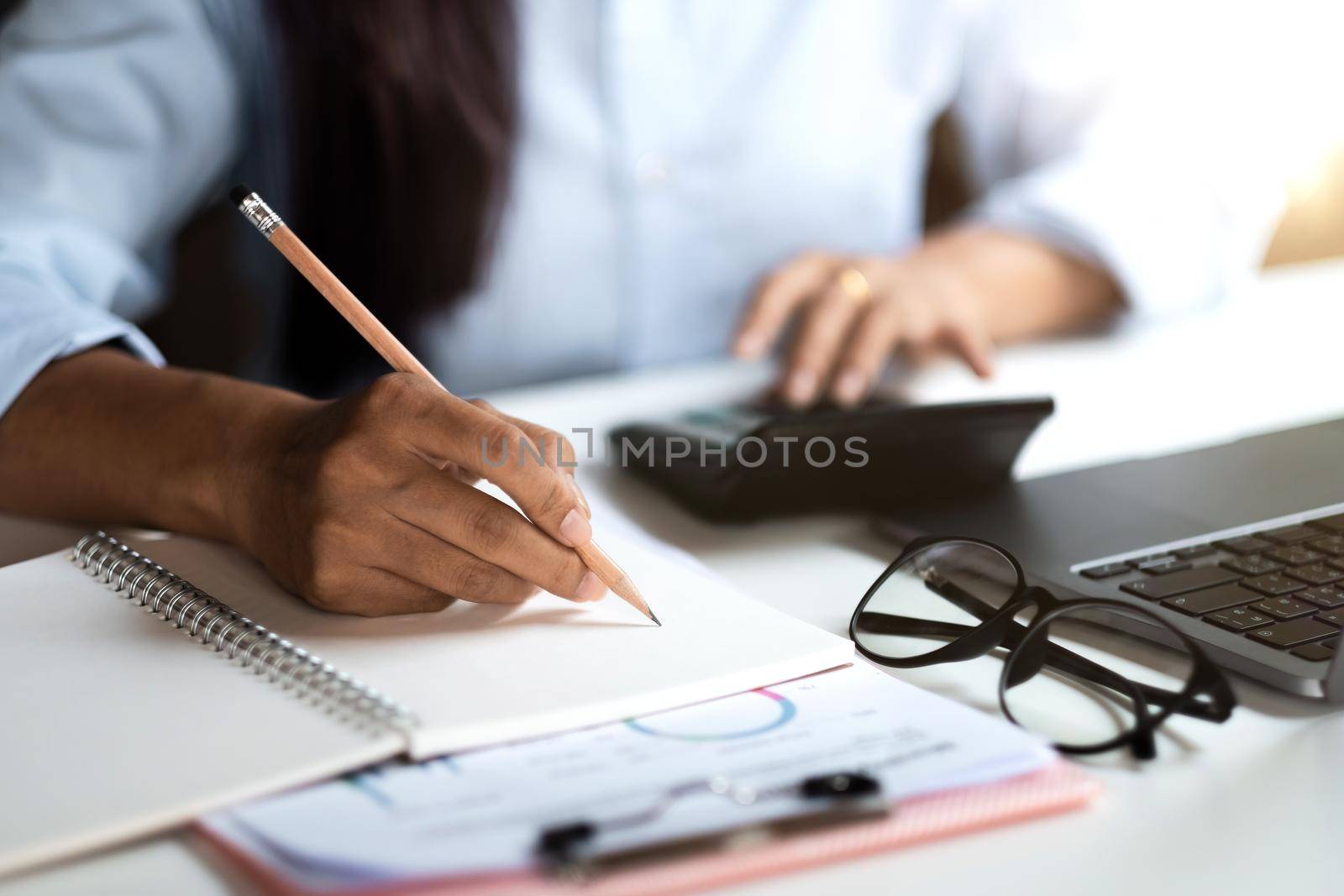 Close up of businessman or accountant hand holding pen working on calculator and laptop computer to calculate business data during make note at notepad, accountancy document at office by nateemee