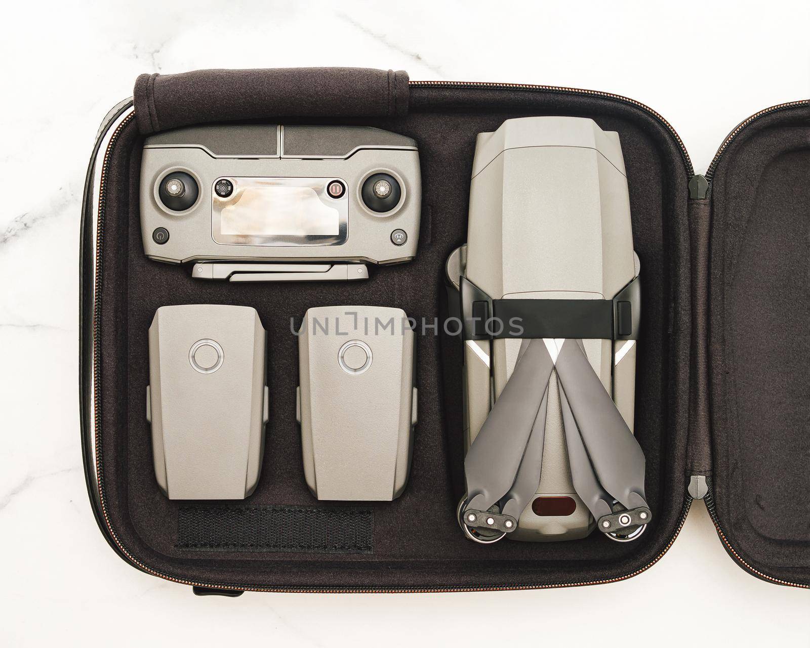 Folding drone quadcopter with full set in case. Top view or flat lay. Kit of drone UAV and accessories - controller and two battary in case over white marble background