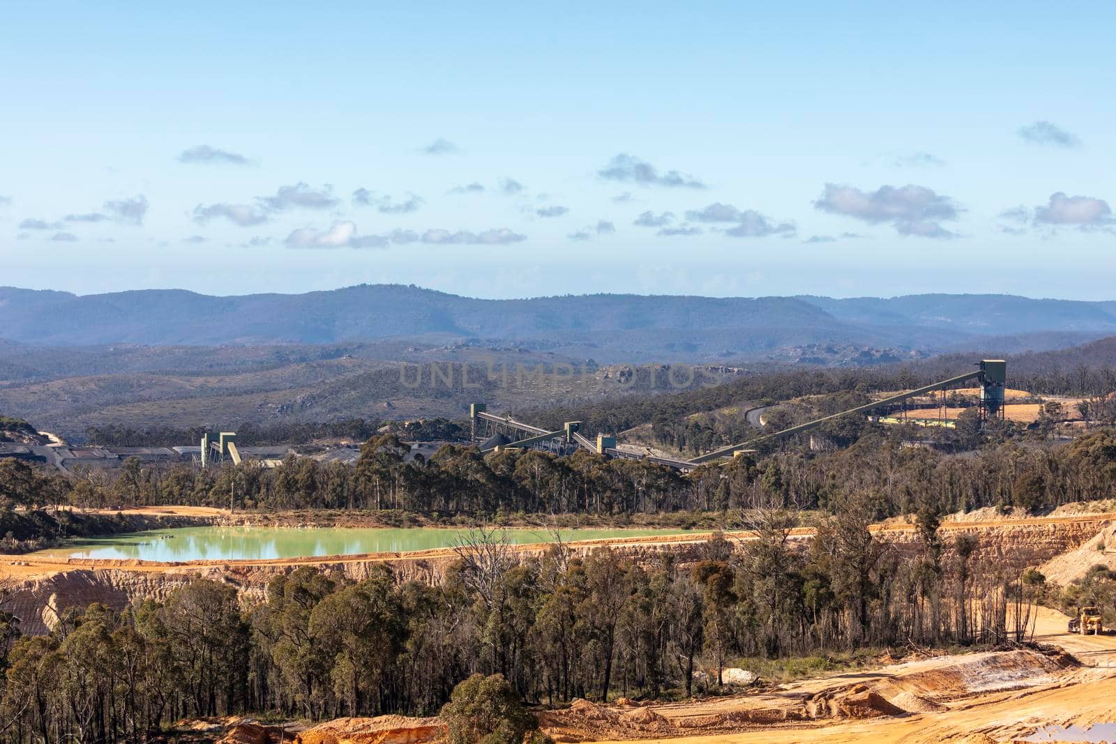 Photograph of transport conveyors in a large colliery surrounded by piles of coal located within a forest