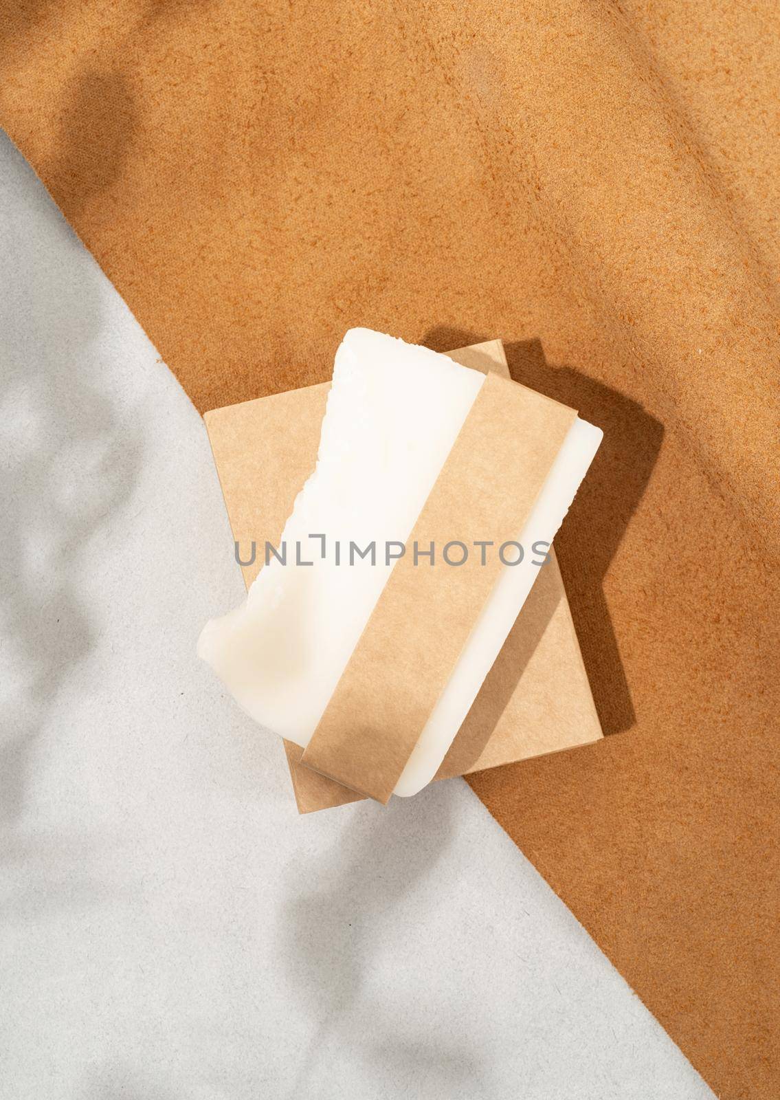 Natural organic cosmetics. Top view of handmade soap with craft blank band on double textured leather background with eucalyptus shadow