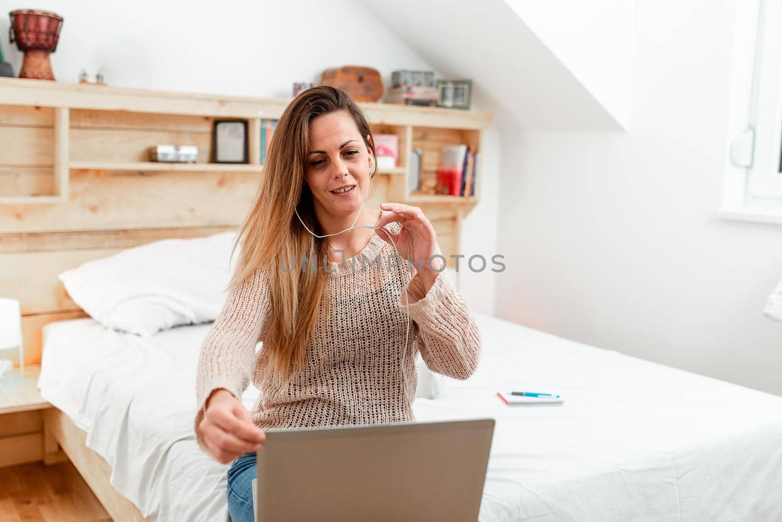 Woman vediocalling through laptop from bedroom with wired headphones