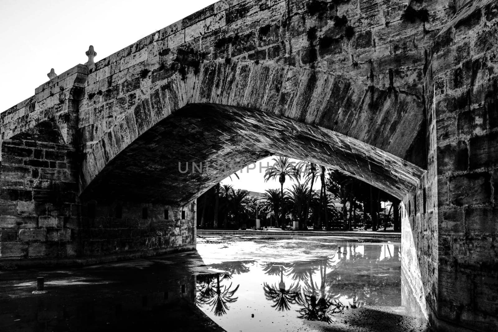 Old Stone bridge and reflections in a park puddle in Valencia