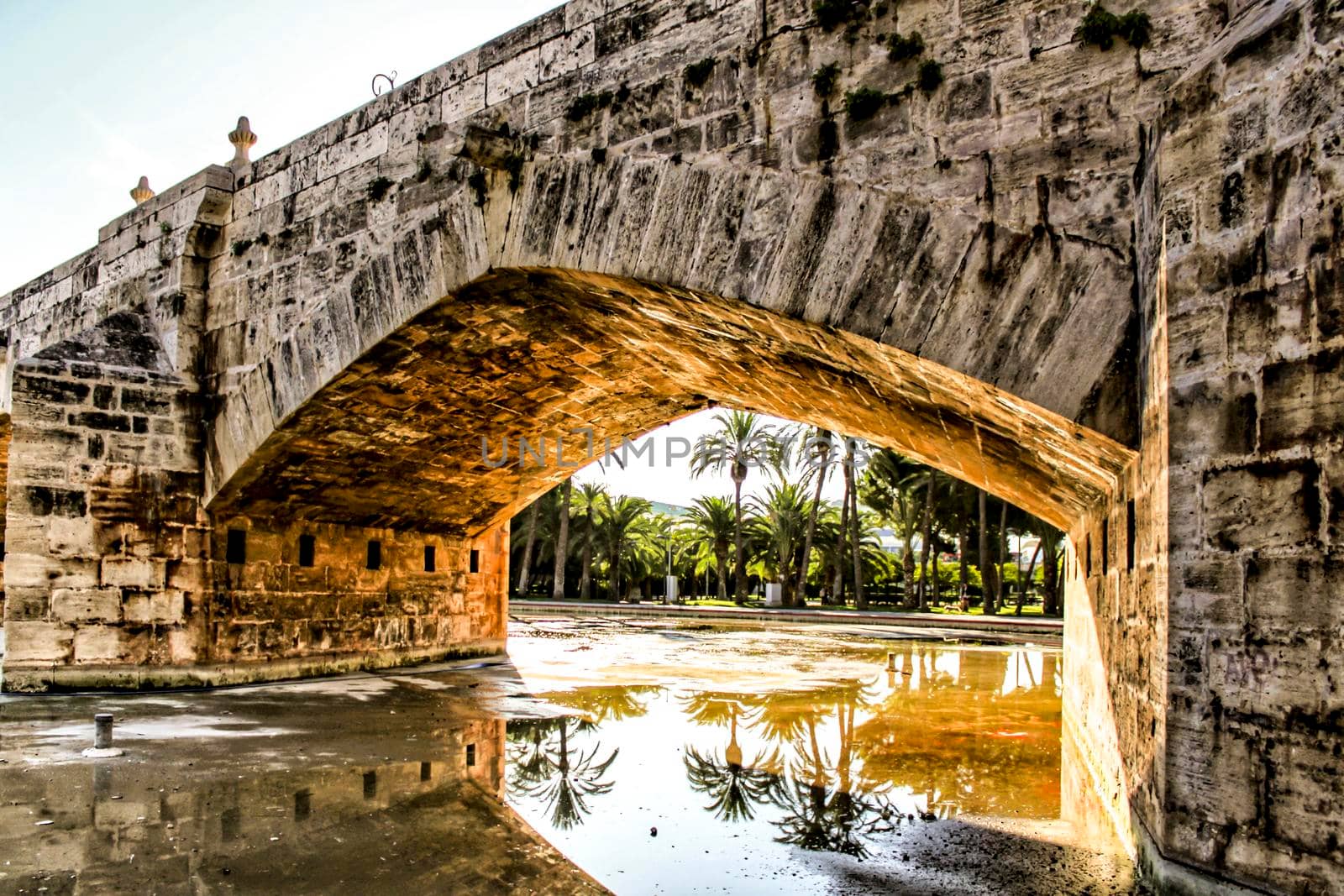 Old Stone bridge and reflections in a park puddle in Valencia