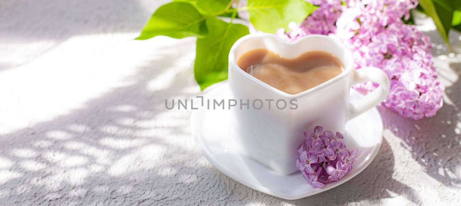 Cappuccino coffee in a cup and a branch of lilac on a white background with shadows . A hot drink. relax. The concept of cafeteria advertising. Article about cappuccino. Making cappuccino. Lilac branches. Spring. Copy space