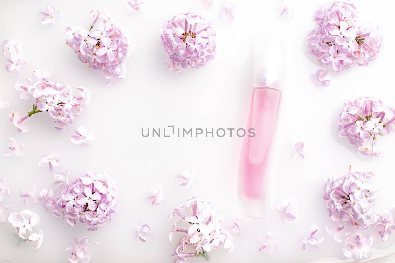 Pink perfume bottle and lilac branch on a white background. The concept of advertising perfumes. A bottle of perfume without text. Floral aromatherapy layout . Copy space