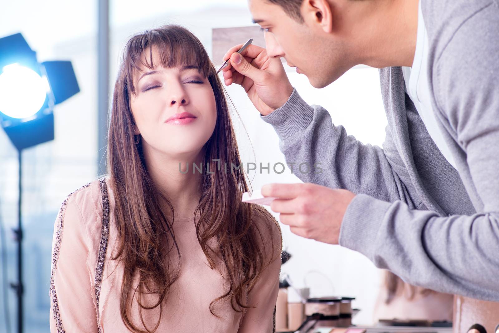 Man doing make-up for cute woman in beauty salon