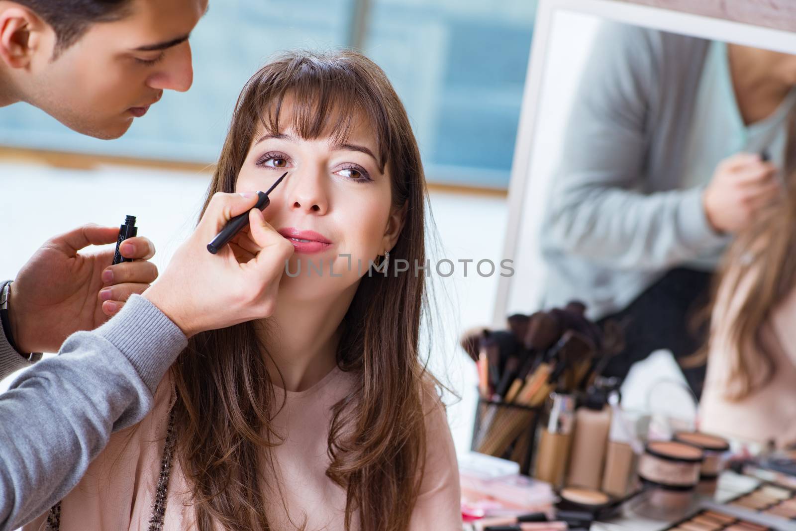 Man doing make-up for cute woman in beauty salon