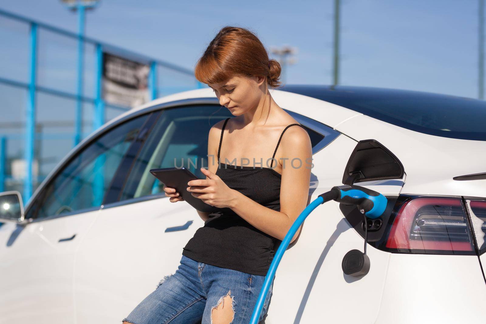 Girl working on tablet while her electric car is charging.