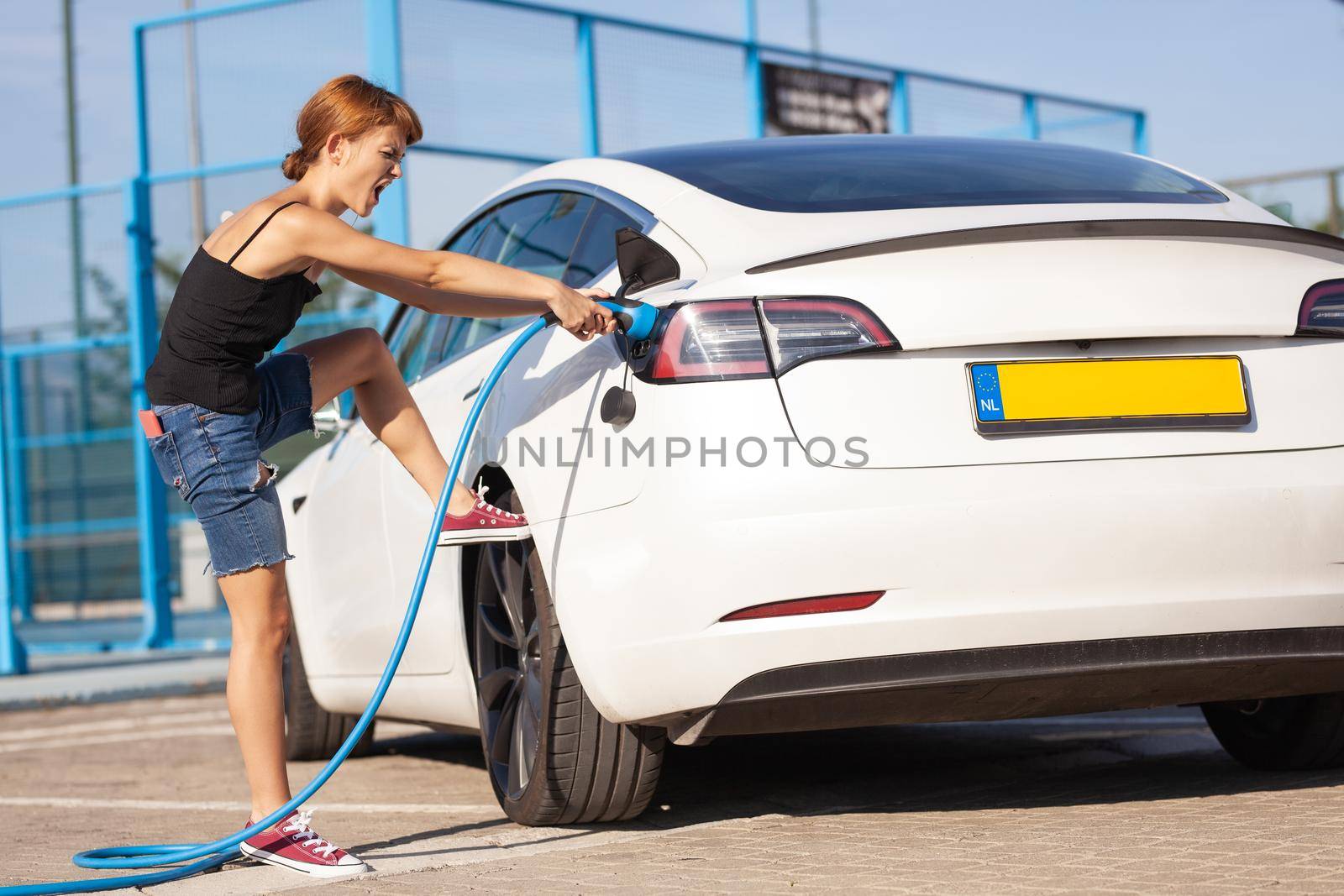 Girl having trouble removing a charging cable from her electric car.