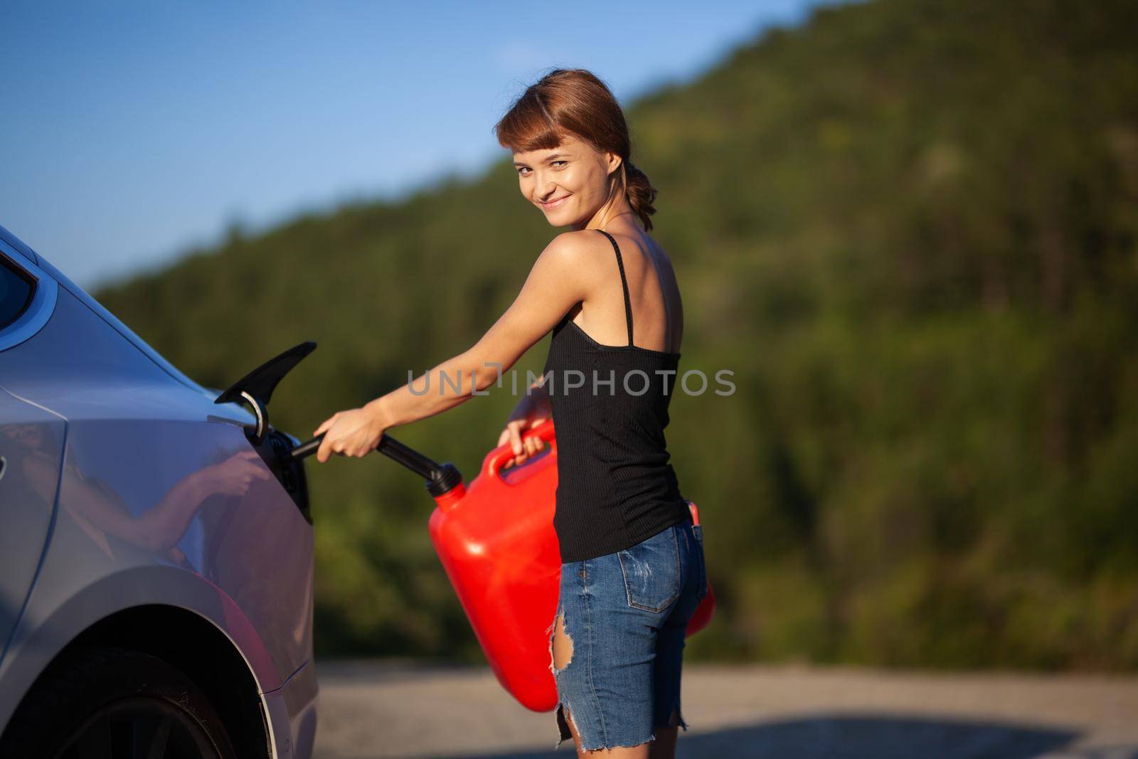 Confused girl trying to put gasoline from a red canister to an empty electric car charging socket.