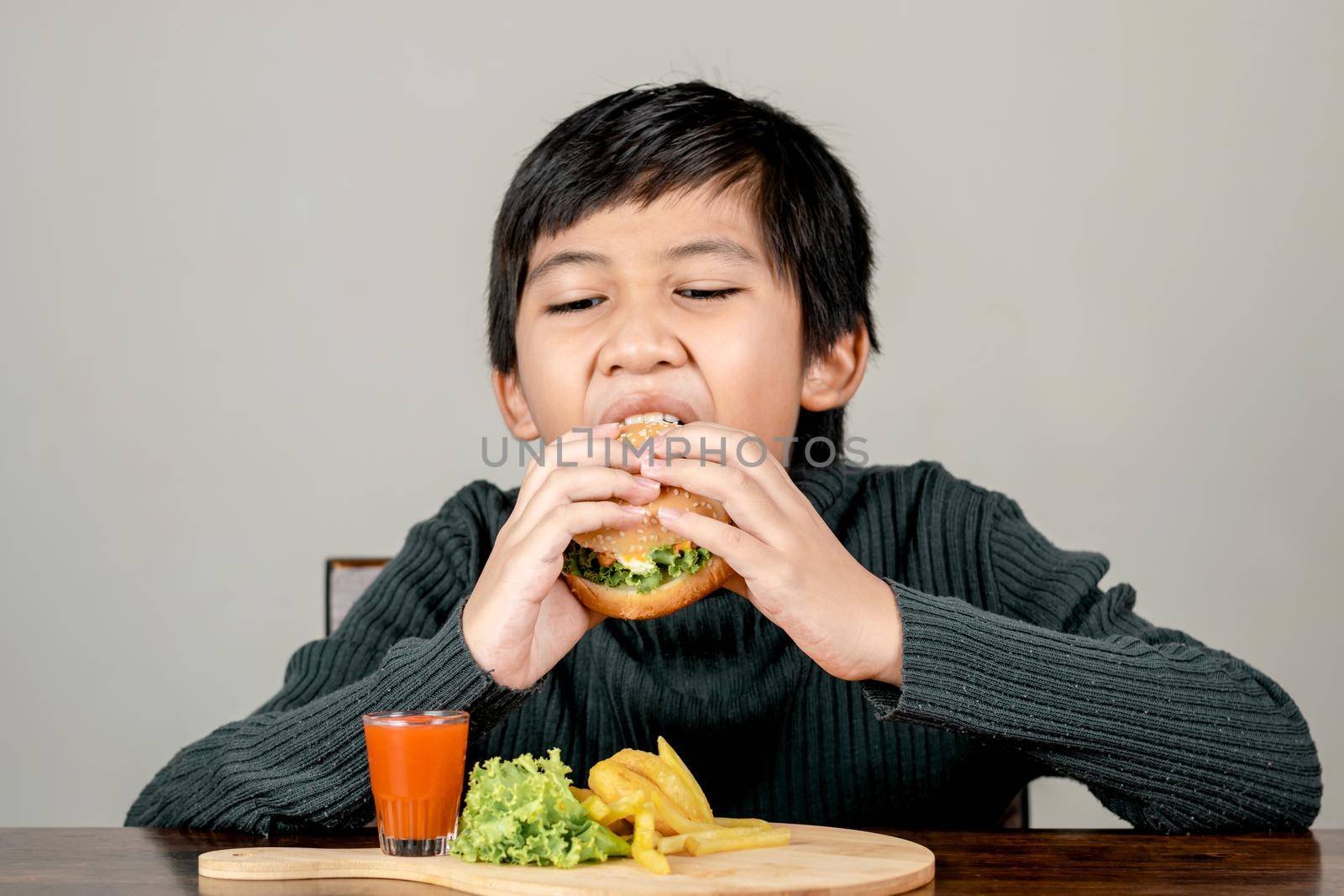 Cute Asian boy eating a delicious hamburger with happiness
