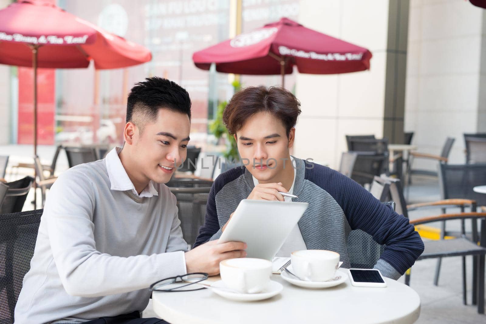Two young handsome businessmen in casual clothes smiling, talking in coffee shop.