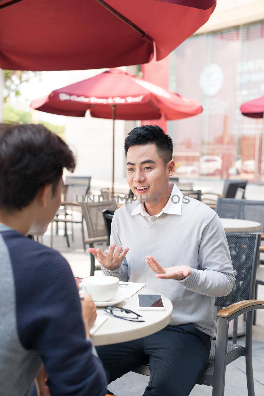 Two young handsome businessmen in casual clothes smiling, talking, drinking coffee while working in office